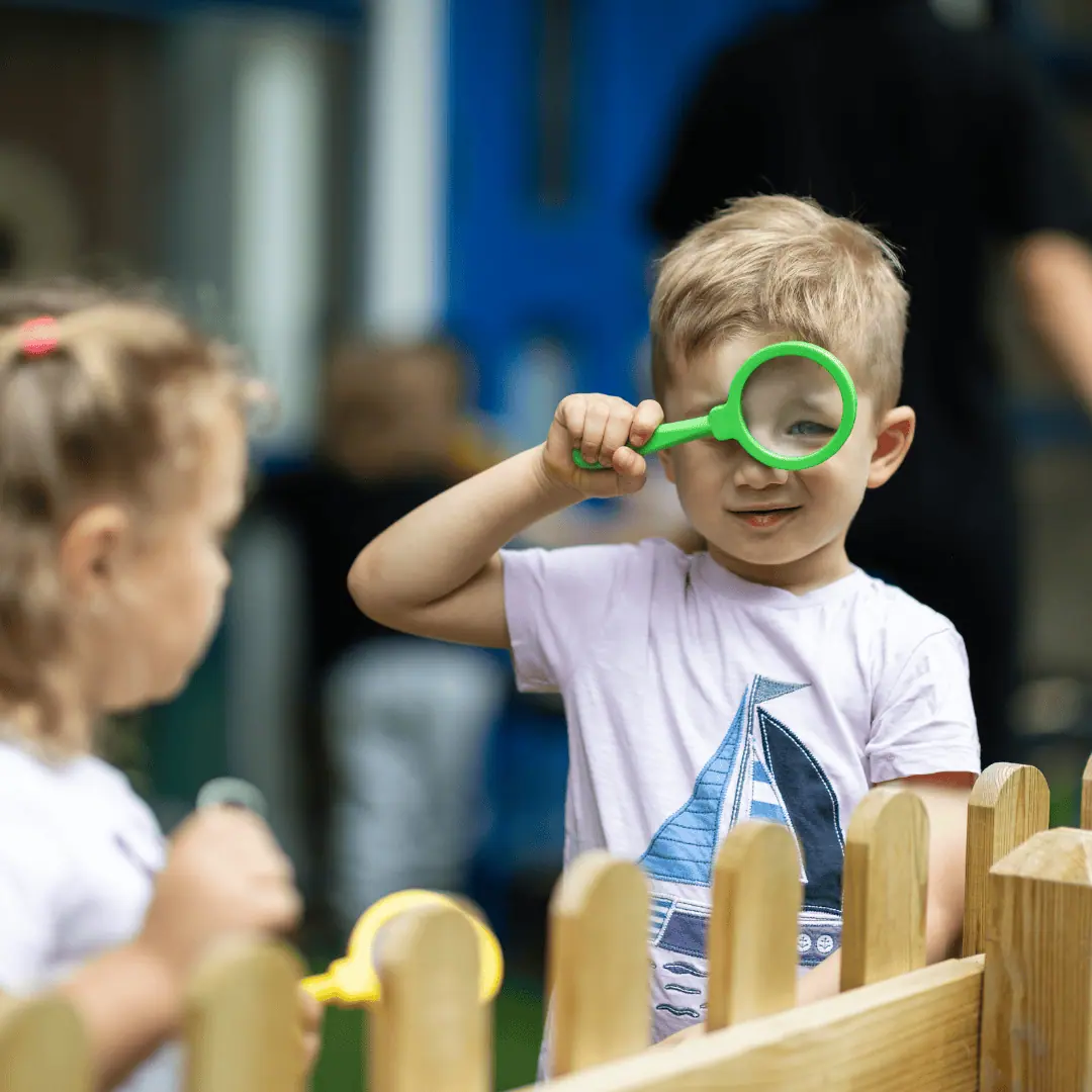 Monkey Puzzle extracurricular activities Child boy using a magnifying glass at Monkey Puzzle Day Nursery Enfield, engaging in outdoor exploration and learning activities.